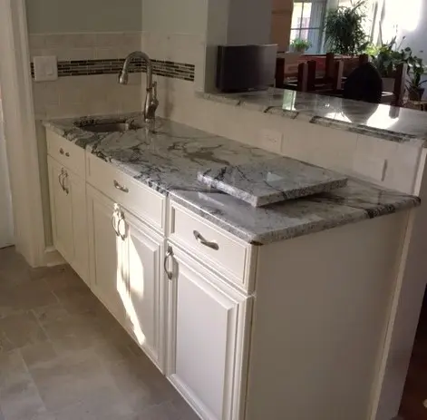 A kitchen with white cabinets and marble counter tops.