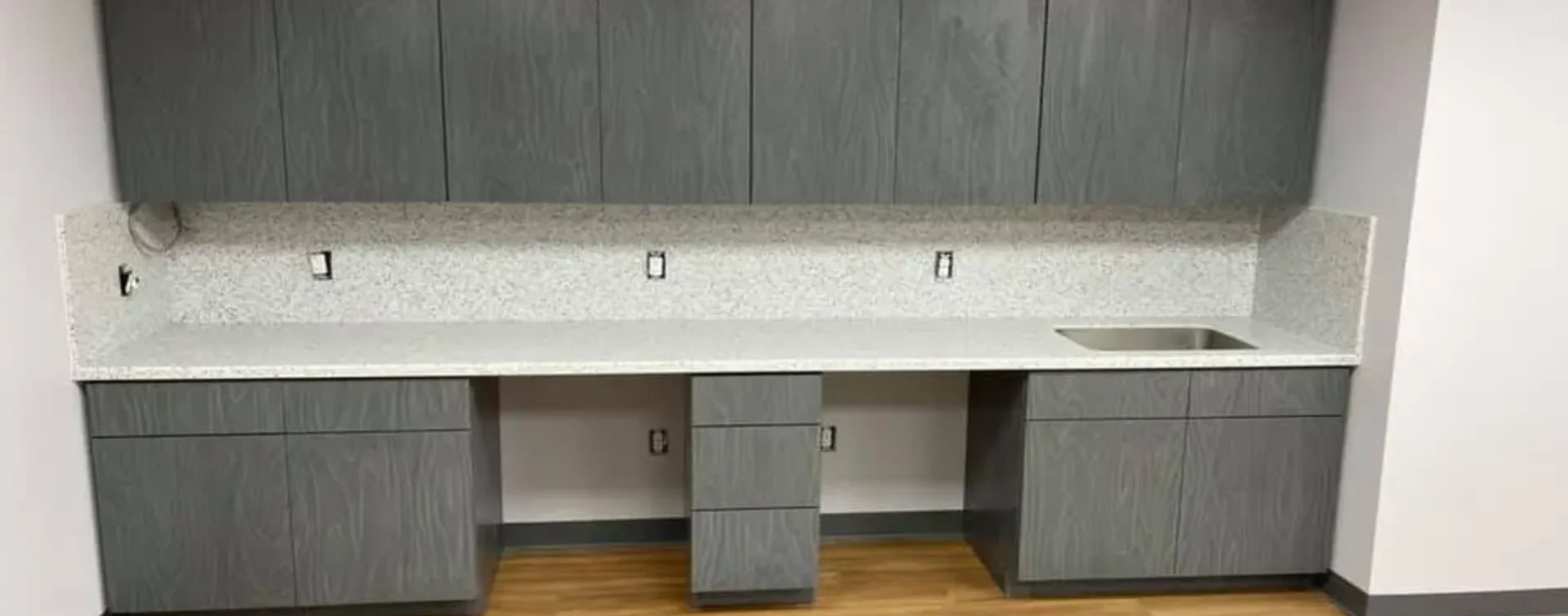 A kitchen with grey cabinets and white counter tops.